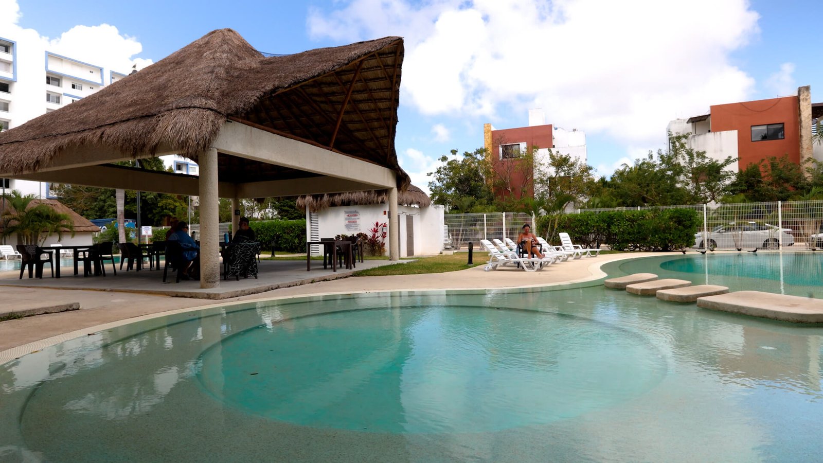 Tener un departamento en Cancún: áreas comunes de un condominio con alberca, palapa, cancha deportiva y áreas verdes